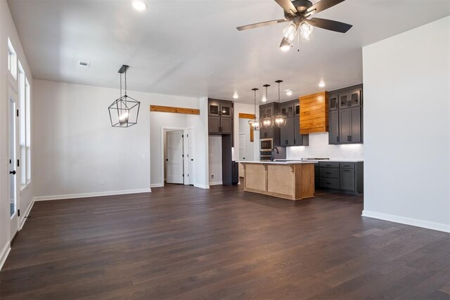 kitchen with pendant lighting, a kitchen island with sink, sink, dark hardwood / wood-style floors, and ceiling fan