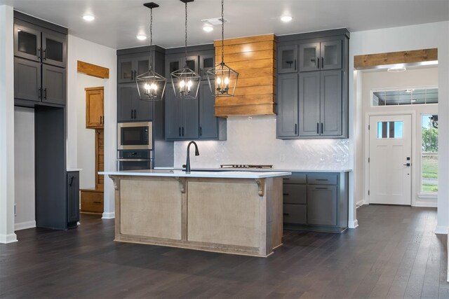 kitchen featuring a center island with sink, pendant lighting, dark wood-type flooring, and appliances with stainless steel finishes