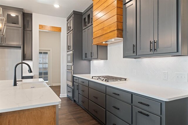 kitchen with premium range hood, sink, light stone counters, dark hardwood / wood-style flooring, and stainless steel appliances