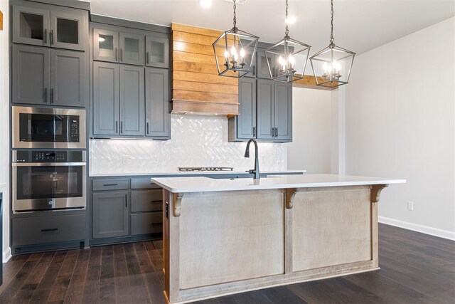 kitchen with appliances with stainless steel finishes, a center island with sink, dark hardwood / wood-style floors, and pendant lighting