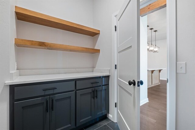 interior space featuring gray cabinetry, dark wood-type flooring, an inviting chandelier, light stone countertops, and decorative light fixtures