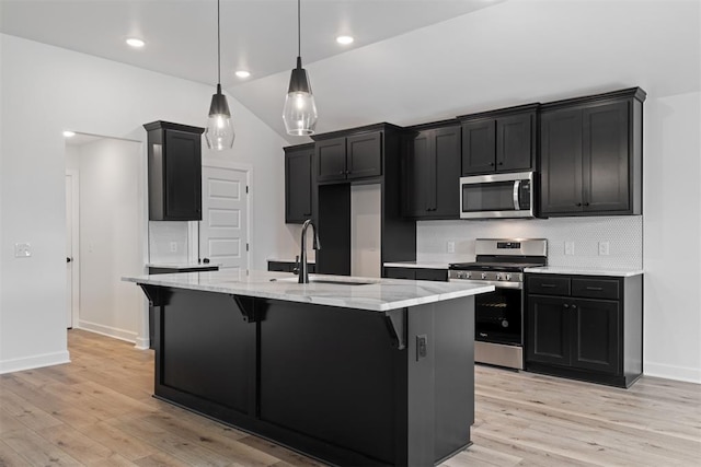 kitchen with appliances with stainless steel finishes, light wood-type flooring, sink, hanging light fixtures, and an island with sink