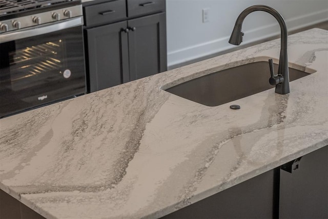 interior details featuring high end range, gray cabinets, light stone counters, and sink