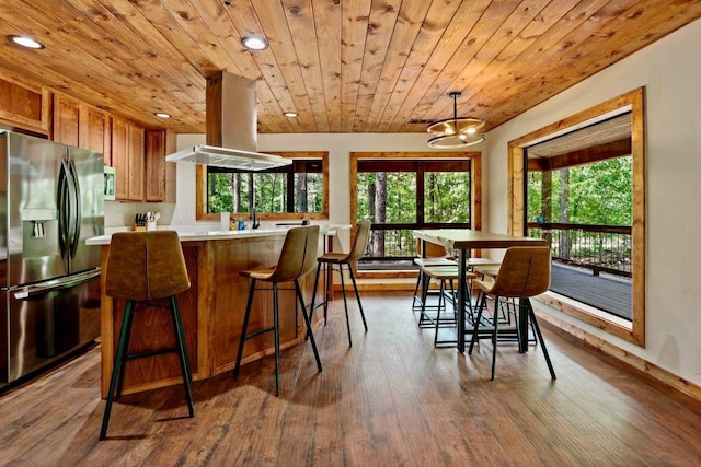 kitchen featuring a healthy amount of sunlight, wood-type flooring, stainless steel fridge with ice dispenser, and island range hood