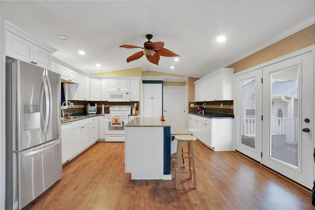 kitchen featuring white appliances, white cabinets, vaulted ceiling, a kitchen island, and a kitchen bar