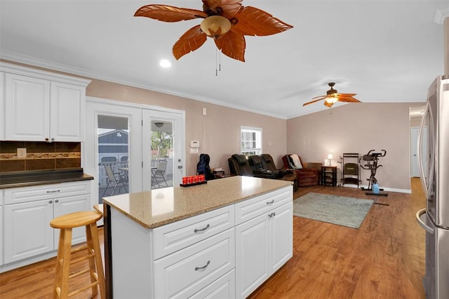 kitchen featuring stainless steel fridge, light wood-type flooring, backsplash, white cabinets, and a breakfast bar area