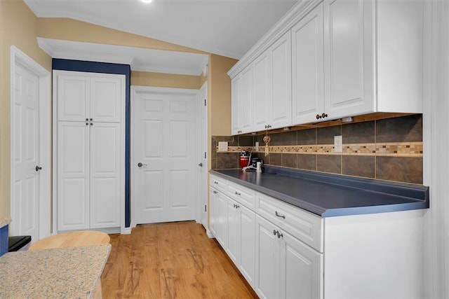 kitchen with white cabinetry, backsplash, light hardwood / wood-style floors, vaulted ceiling, and ornamental molding