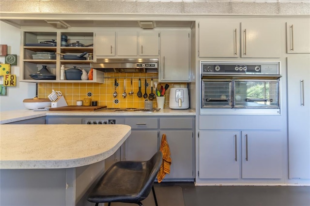 kitchen with a kitchen bar, black oven, tasteful backsplash, and exhaust hood
