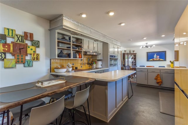 kitchen featuring backsplash, kitchen peninsula, a breakfast bar area, and gray cabinetry