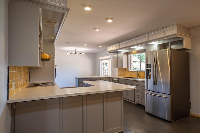 kitchen featuring kitchen peninsula, tasteful backsplash, cooktop, sink, and stainless steel fridge with ice dispenser