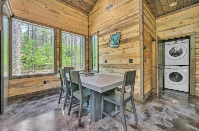 dining space featuring wood walls, high vaulted ceiling, wood ceiling, and stacked washer / drying machine