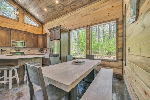 dining room with wood walls, a healthy amount of sunlight, wood ceiling, and high vaulted ceiling