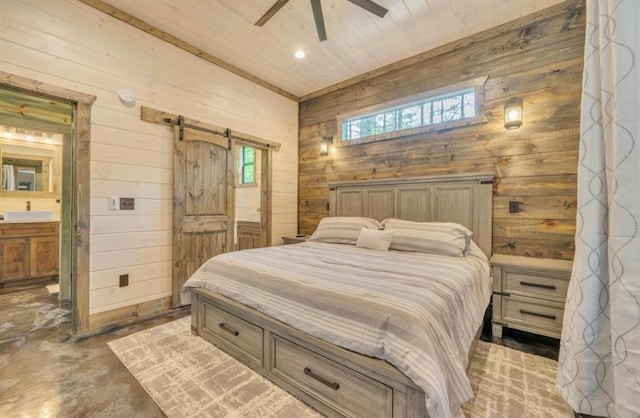 bedroom featuring a barn door, ceiling fan, wooden walls, and ensuite bath