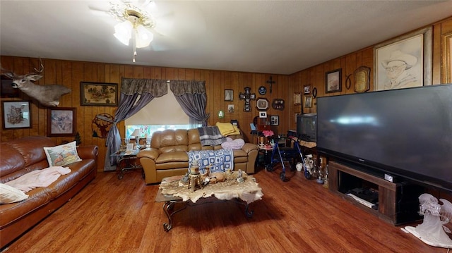 living room with ceiling fan, wood walls, and light wood-type flooring