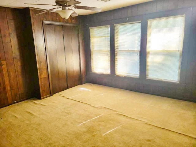 unfurnished room with carpet flooring, ceiling fan, and wooden walls