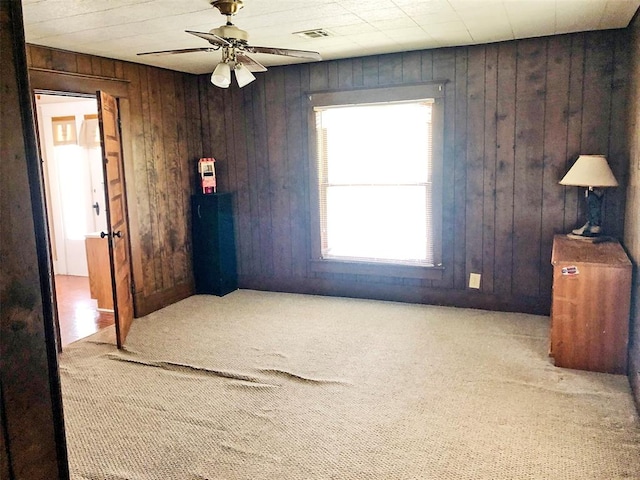 empty room featuring wood walls, carpet floors, and ceiling fan