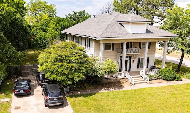 view of front of property with a front yard, a shingled roof, covered porch, fence, and a balcony