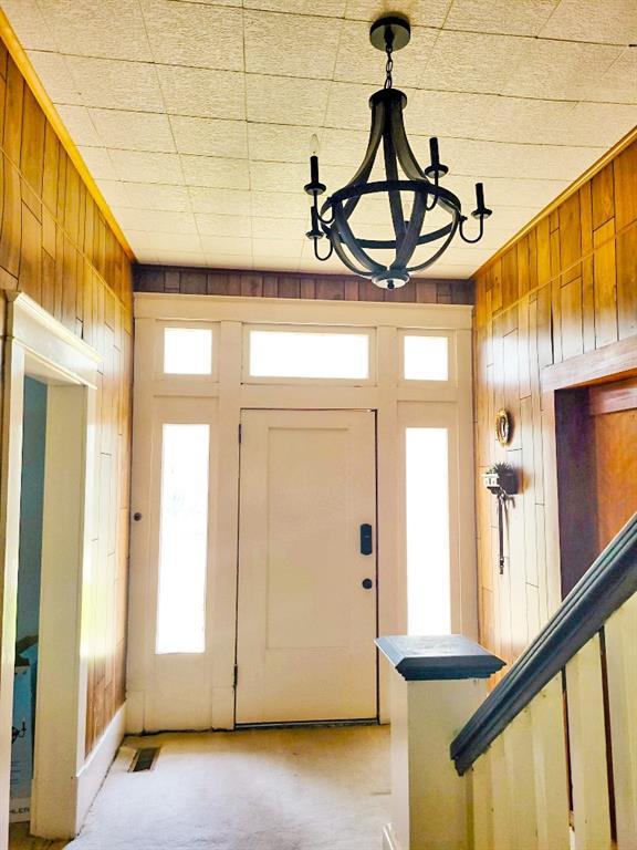 entryway featuring wood walls, a notable chandelier, light carpet, and visible vents