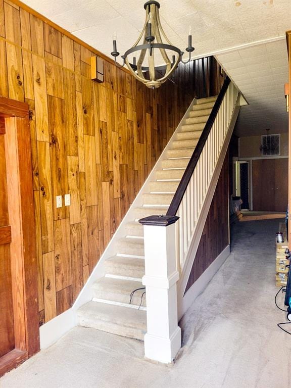 stairway featuring wooden walls, a notable chandelier, and carpet flooring
