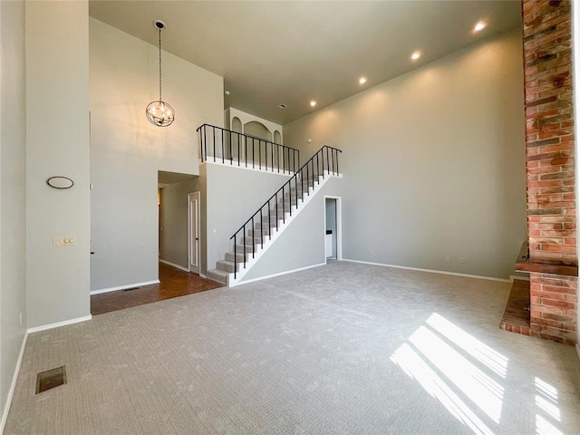 unfurnished living room with an inviting chandelier, a towering ceiling, and dark colored carpet