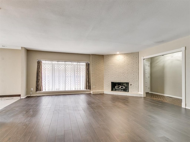 unfurnished living room featuring dark hardwood / wood-style floors, a textured ceiling, and a brick fireplace