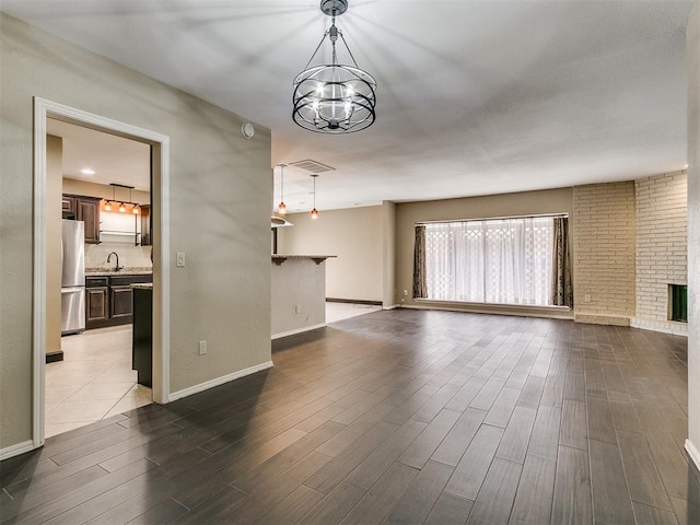 unfurnished living room featuring sink, dark hardwood / wood-style flooring, a fireplace, and a chandelier