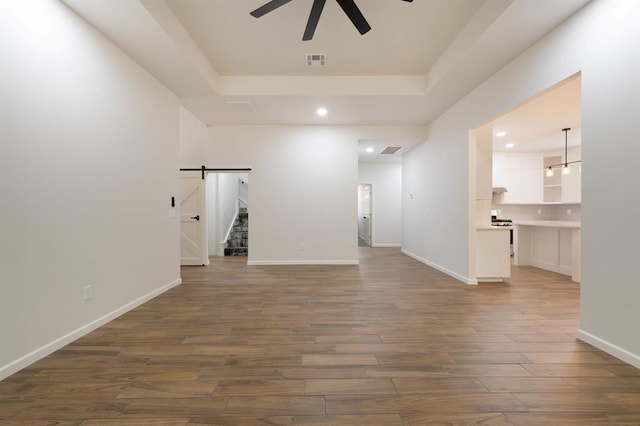 interior space featuring a raised ceiling, a barn door, ceiling fan, and dark wood-type flooring