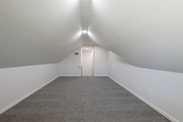 additional living space featuring dark carpet and vaulted ceiling