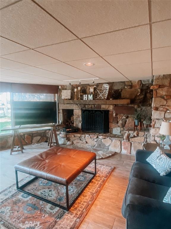 living room featuring a stone fireplace, a paneled ceiling, and hardwood / wood-style flooring