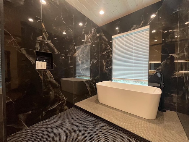 bathroom with a tub to relax in and tile walls