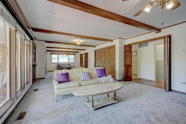 living room with beamed ceiling, light colored carpet, ceiling fan, and ornamental molding