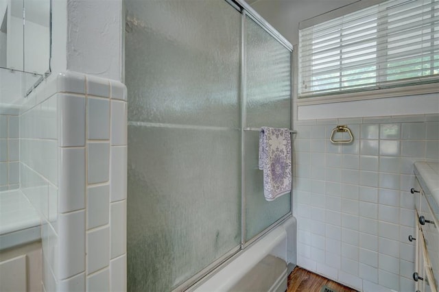 bathroom featuring combined bath / shower with glass door, wood-type flooring, and tile walls