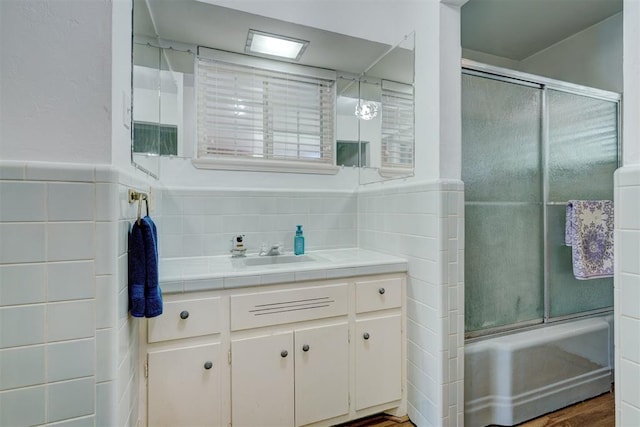 bathroom featuring hardwood / wood-style flooring, vanity, enclosed tub / shower combo, and tile walls