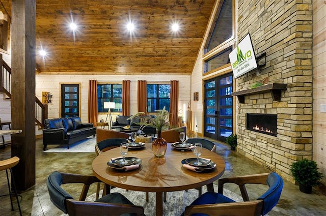 dining room featuring a stone fireplace, wood walls, high vaulted ceiling, and wooden ceiling