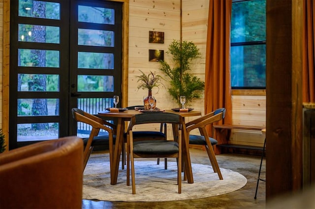 dining space with concrete flooring, french doors, and wooden walls