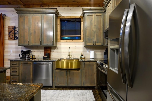 kitchen with wood walls, stainless steel appliances, sink, and dark stone countertops