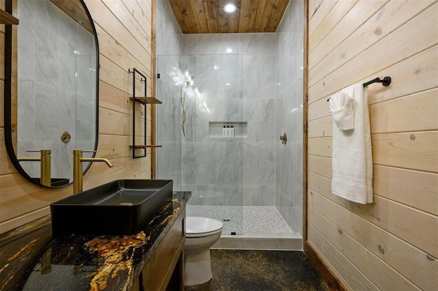 bathroom with a tile shower, wood walls, vanity, wood ceiling, and toilet