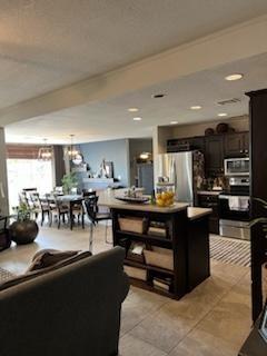 kitchen with dark brown cabinetry, light tile patterned floors, an inviting chandelier, a kitchen island, and appliances with stainless steel finishes