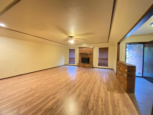 unfurnished living room with ceiling fan, light hardwood / wood-style floors, a textured ceiling, and a brick fireplace