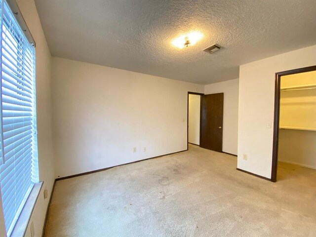 unfurnished bedroom with a walk in closet, a textured ceiling, light carpet, and a closet