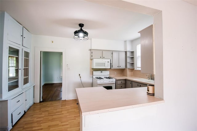 kitchen with kitchen peninsula, white appliances, sink, gray cabinets, and light hardwood / wood-style floors