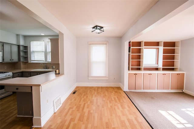 kitchen featuring sink, kitchen peninsula, stove, light hardwood / wood-style floors, and gray cabinets