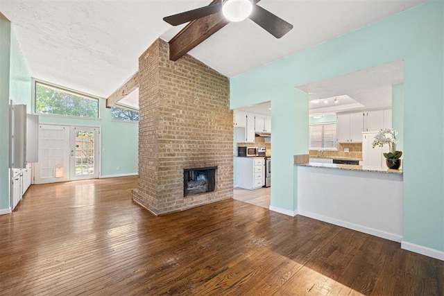 unfurnished living room with beamed ceiling, hardwood / wood-style flooring, a brick fireplace, and ceiling fan