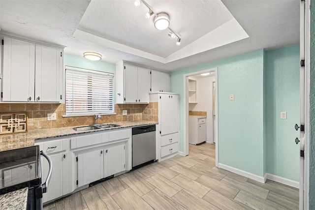 kitchen featuring white cabinets, a tray ceiling, stainless steel dishwasher, and sink