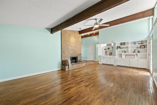 unfurnished living room with a brick fireplace, a textured ceiling, ceiling fan, beam ceiling, and hardwood / wood-style floors