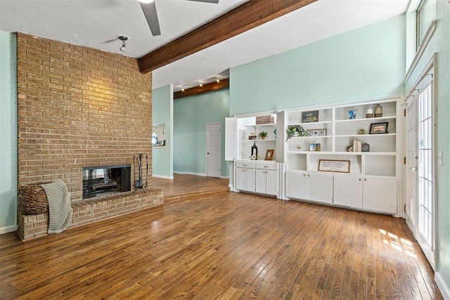 unfurnished living room featuring hardwood / wood-style flooring, beam ceiling, a fireplace, and a wealth of natural light