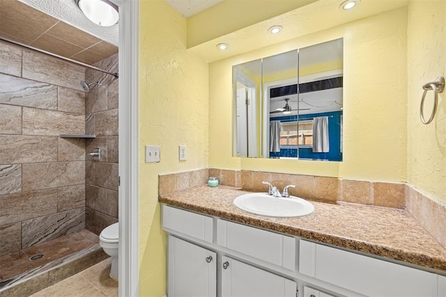 bathroom with a tile shower, vanity, toilet, and ceiling fan