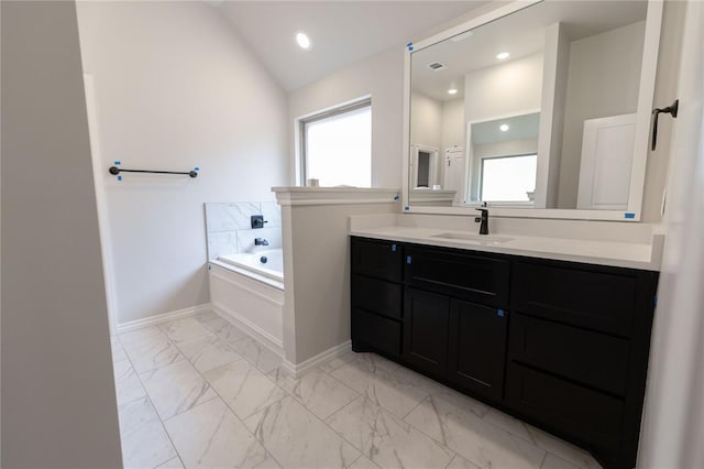 bathroom featuring vaulted ceiling, a tub to relax in, and vanity