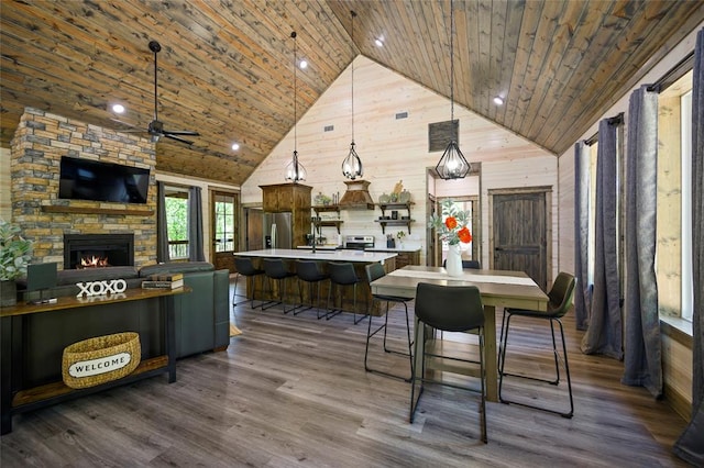 dining area featuring wood walls, wooden ceiling, a fireplace, and high vaulted ceiling