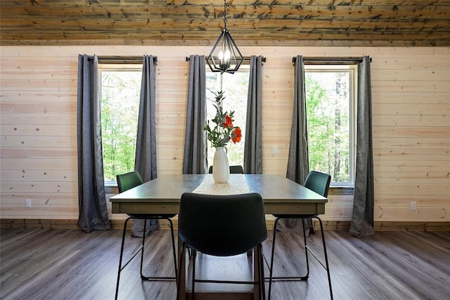 dining area featuring hardwood / wood-style flooring, a healthy amount of sunlight, wooden walls, and an inviting chandelier